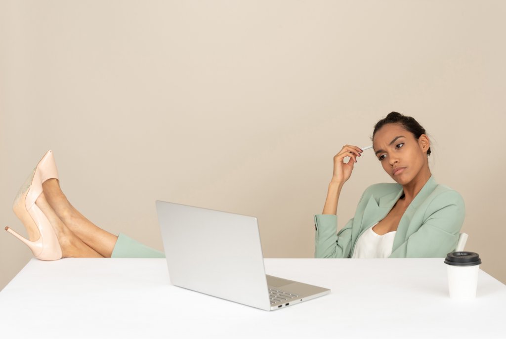 content marketing mistakes - woman in green thinking and working on a laptop with a coffee on the table