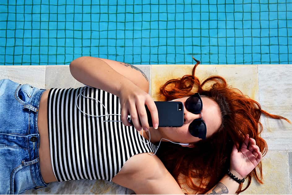 IGTV and Instagram Stories for Lead Generation redhead girl laying next to the swimming pool dressed in jeans and strippes with mobile phone and headphones