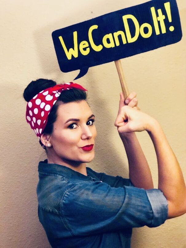 Woman dressed up us Rosie the Riveter holding a "We can do it" banner