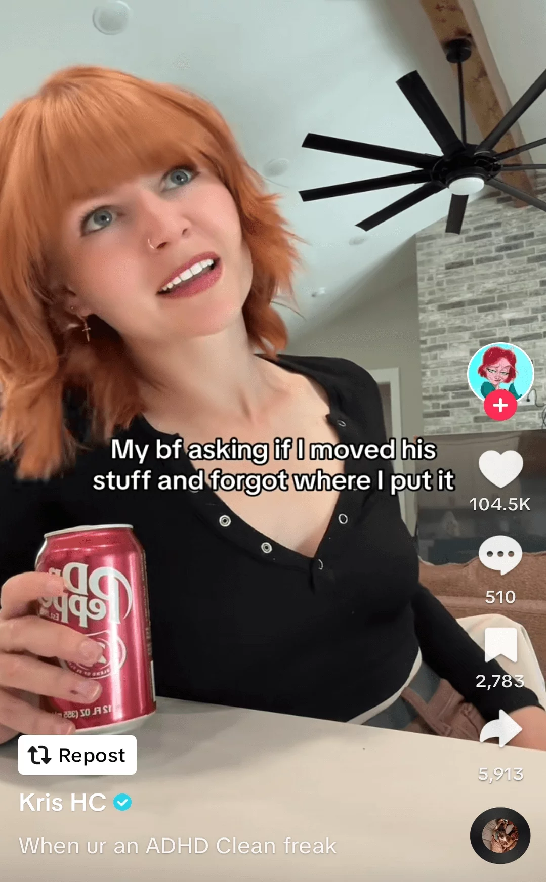 Woman with red hair holding a soda can, making a playful expression in her modern kitchen, featured in a social media post.
