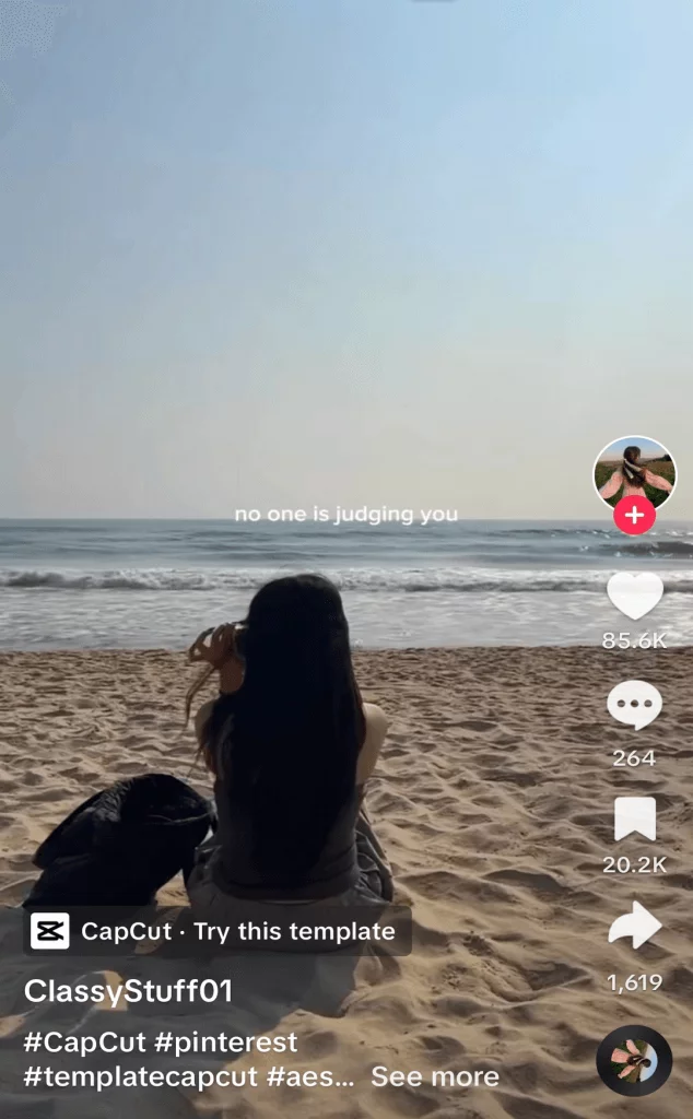 TikTok post of a girl sitting on a sandy beach with her back to camera, captioned 'no one is judging you'.