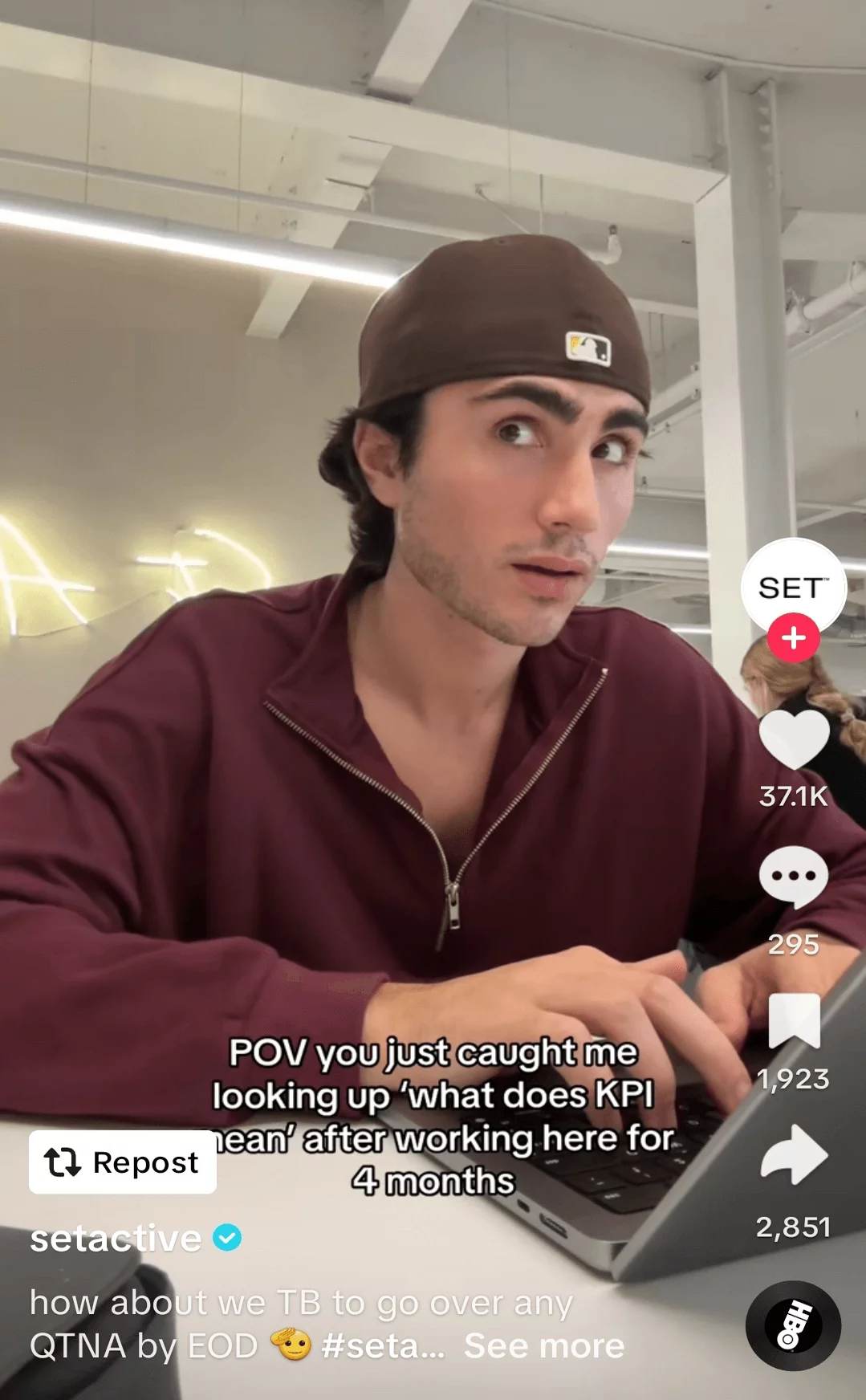 Young man in an office setting looks surprised while using a laptop, captured in a humorous social media video about workplace learning.