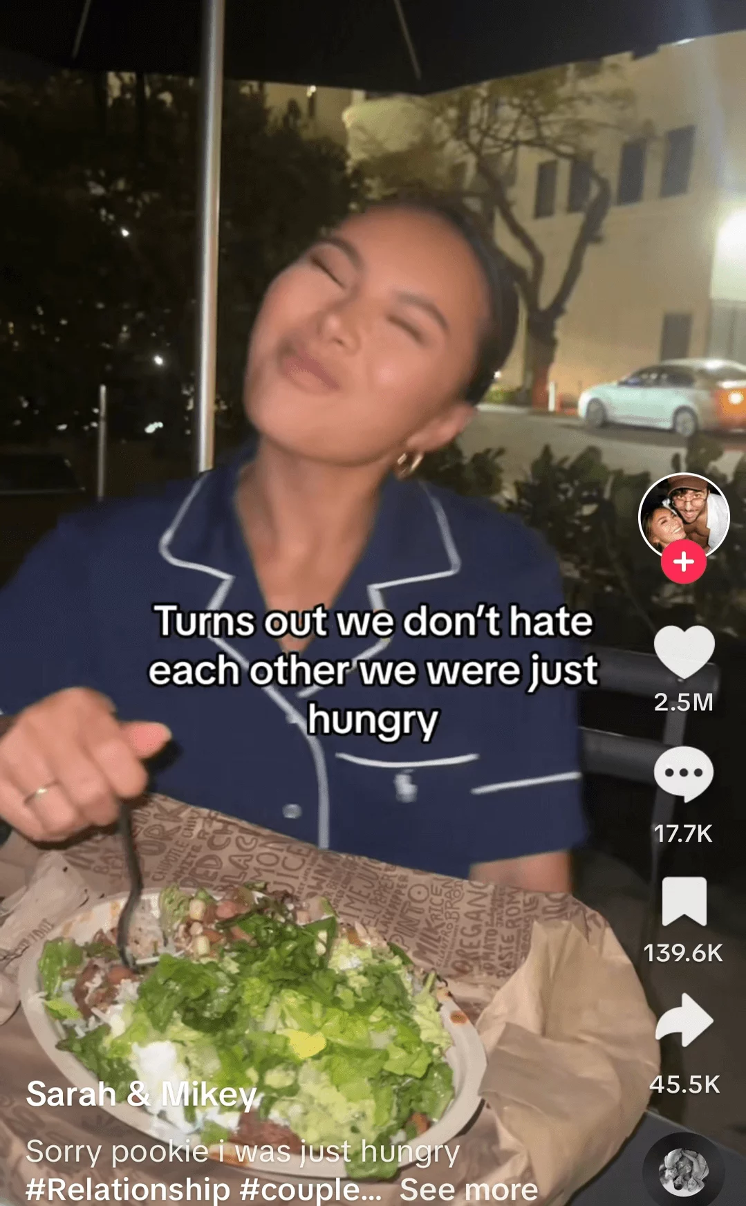 Contented young woman enjoying a salad at an outdoor dining setting, captured in a humorous social media post about hunger and mood.