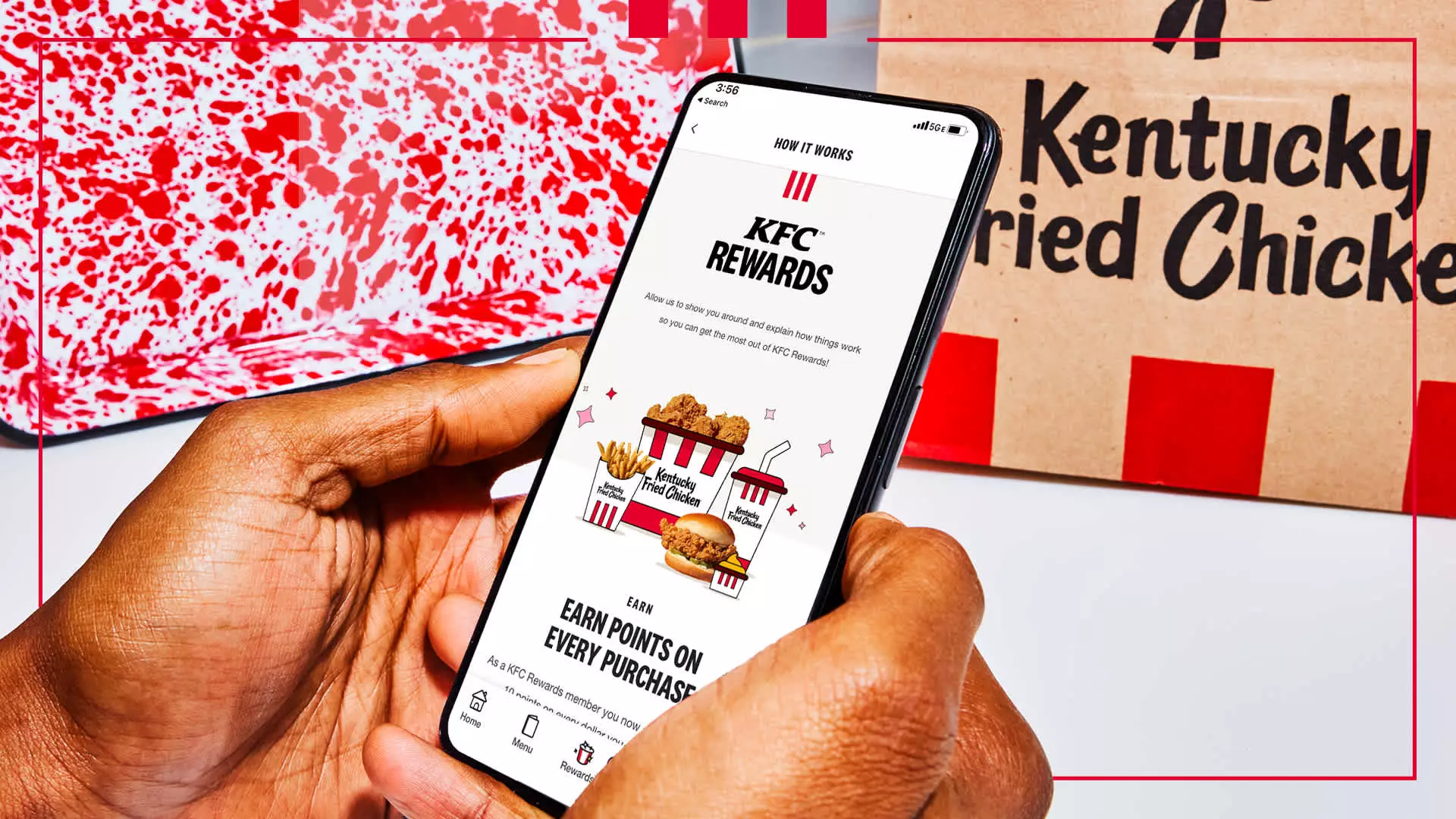 A person holding a phone displaying the KFC Rewards app with a Kentucky Fried Chicken box in the background.