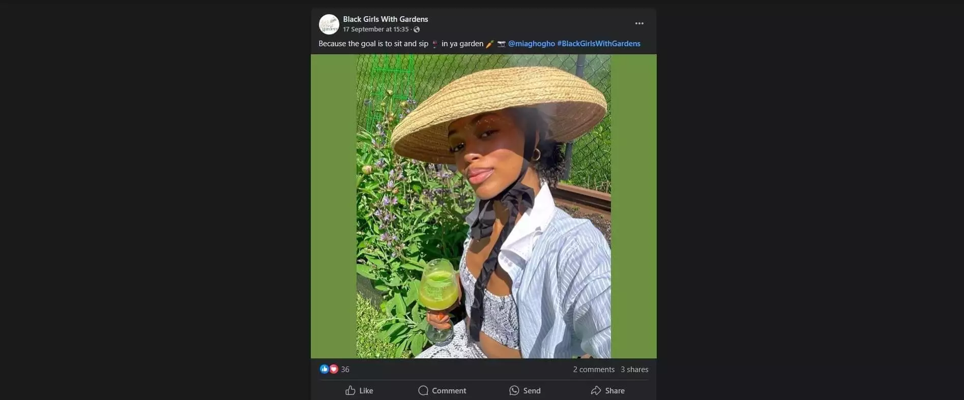 Woman in a garden wearing a straw hat, holding a green drink, enjoying the outdoors with blooming flowers in the background.